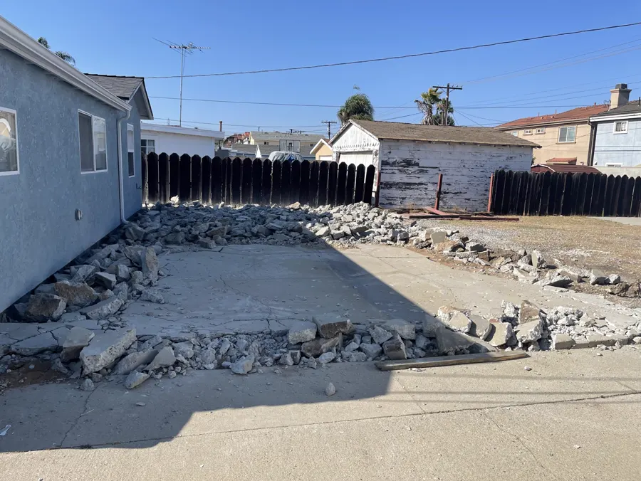 An old driveway broken into rubble beside a blue house