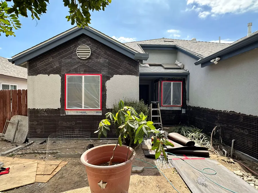 A house wrapped in lath with new windows set, before the stucco coat