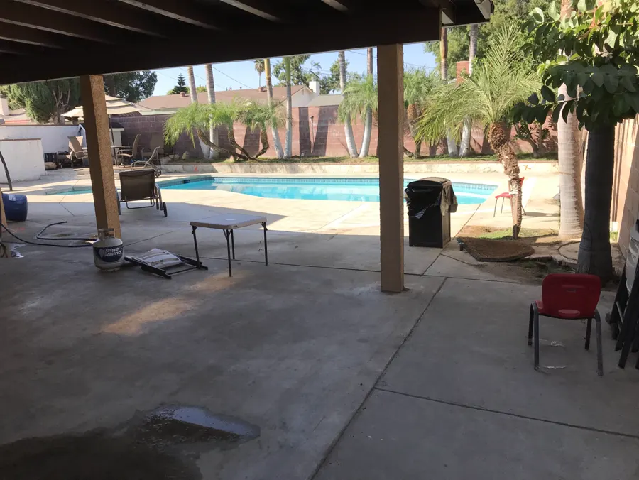 A concrete patio under a wood patio cover beside a pool