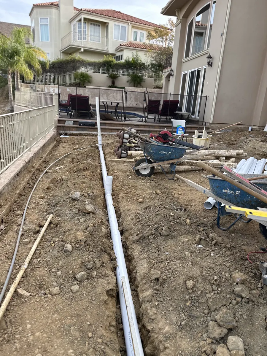 A new drain line laid in the dirt beside a two-story house